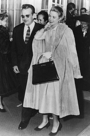 Grace Kelly walking with Prince Rainier, carrying her Hermes Kelly bag, wearing a fur-collared coat