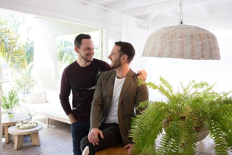 Darren Palmer and Olivier Duvillard laughing together in their light-filled Bondi home among lush ferns