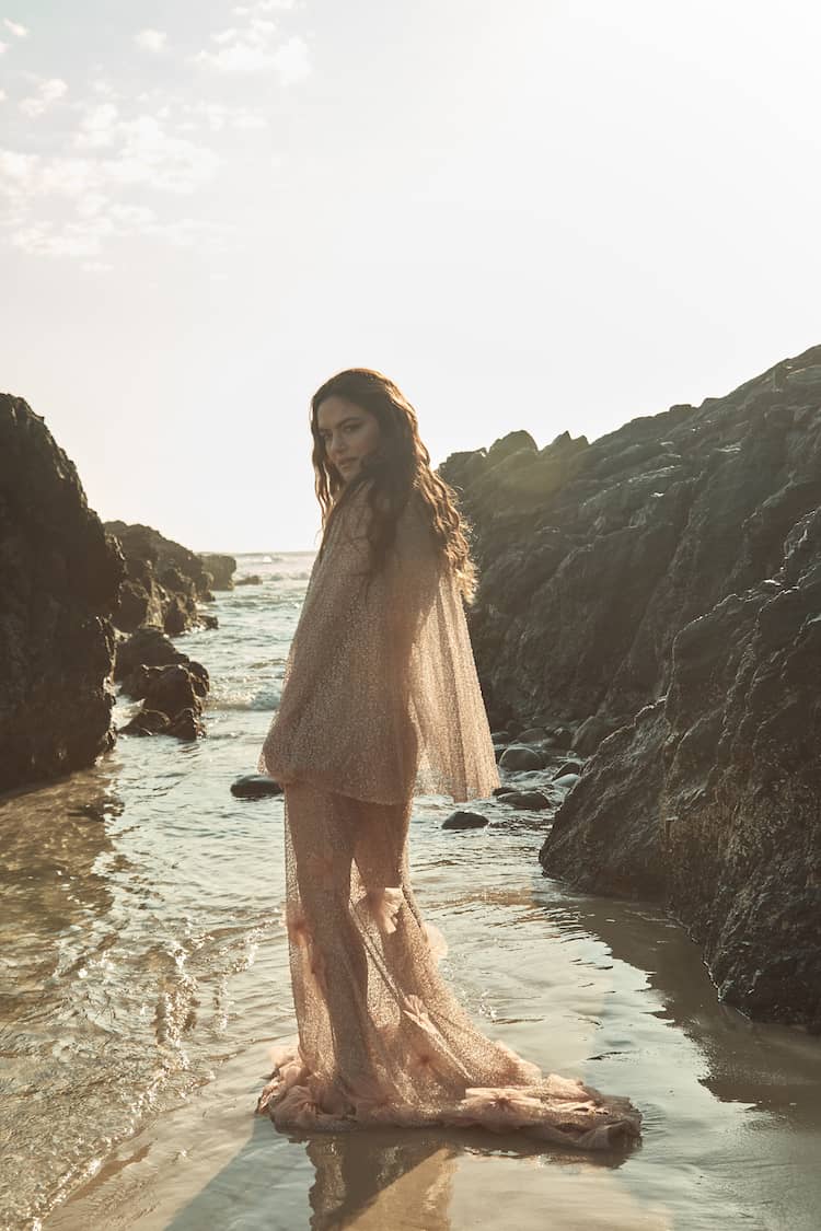 Julia Stone lying on sand, auburn curls fanned out above her head, hand resting near her face in warm light
