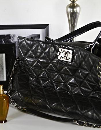 Still life of Chanel quilted bag, framed photos, white roses, Jo Malone candle and perfume on white surface