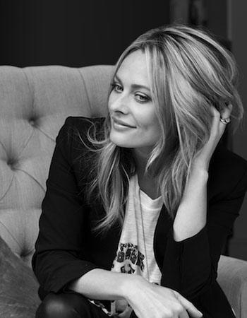 Sarah Jagger at her vanity in a relaxed pose, soft light catching her blonde hair and gold jewellery