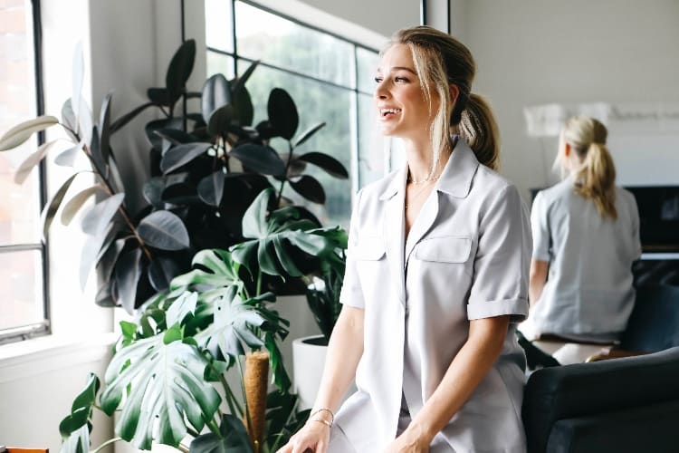 Anna Heinrich in a light grey utility shirt, smiling in profile in a bright plant-filled office