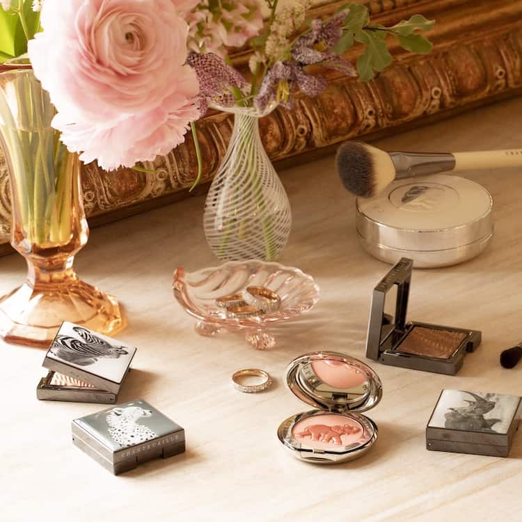 Chantecaille products arranged on a French antique vanity with a gilt mirror, pink roses and crystal vases