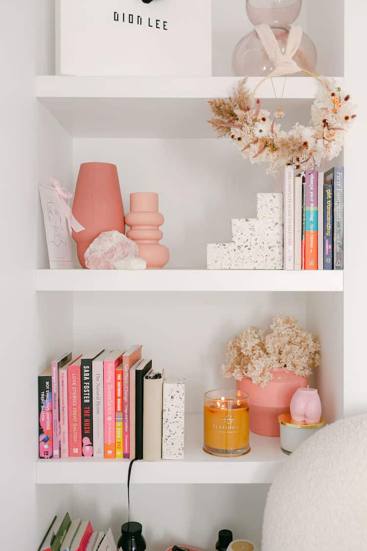 White bookshelf with pink ceramic vases, rose quartz crystal, a Glasshouse candle and dried flowers