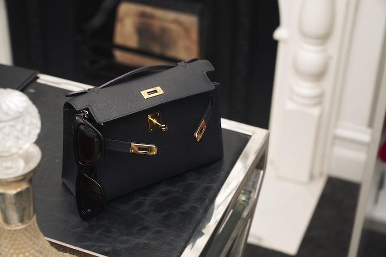 Black leather handbag with gold hardware and tortoiseshell sunglasses on mirrored side table