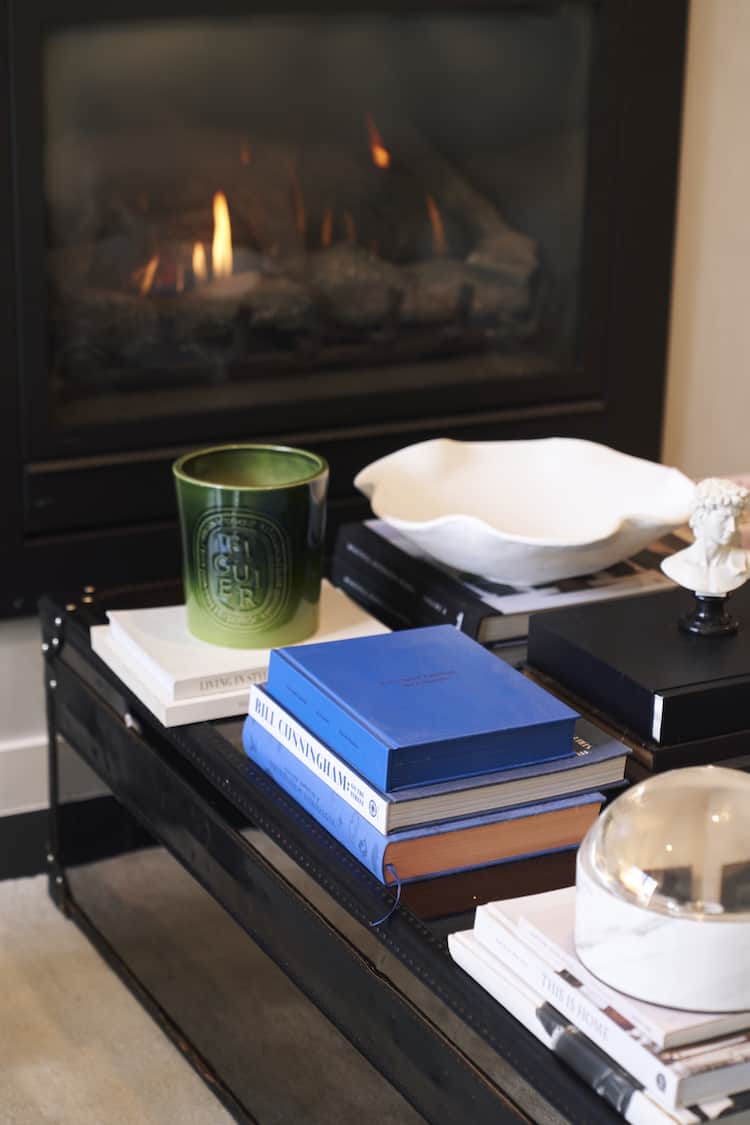 Styled coffee table by fireplace with Diptyque candle, fashion books and ceramic bowl