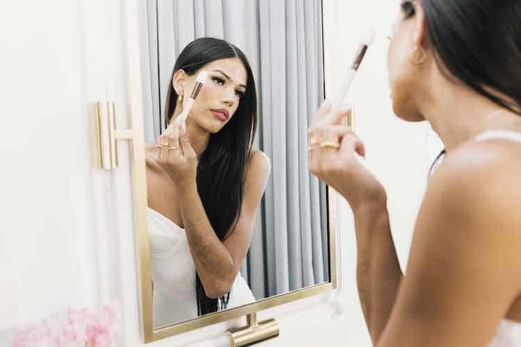 Riley Minford applying highlighter in a bathroom mirror