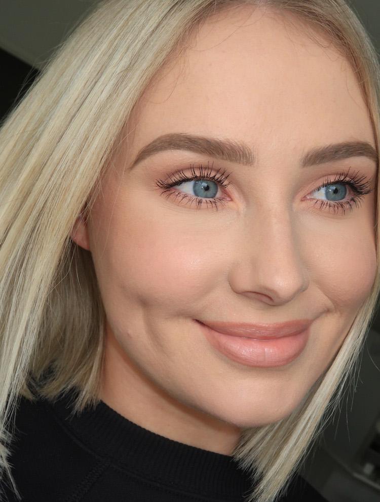 Close-up of Lauren Curtis with a soft peach makeup look, blonde bob and blue eyes, smiling at the camera