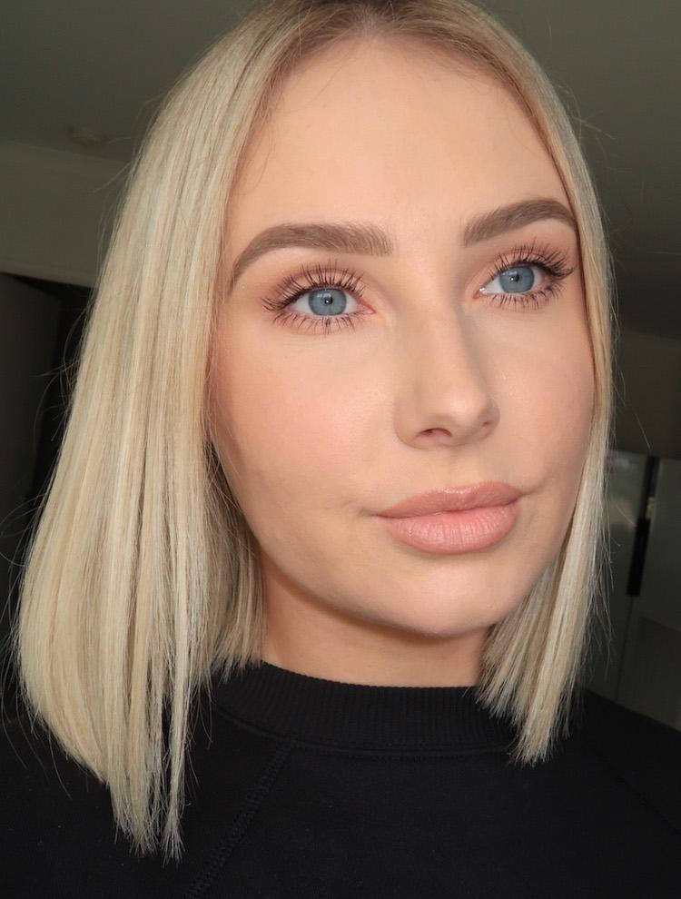 Lauren Curtis with a natural nude lip and bronzed skin, platinum blonde bob, looking directly at the camera