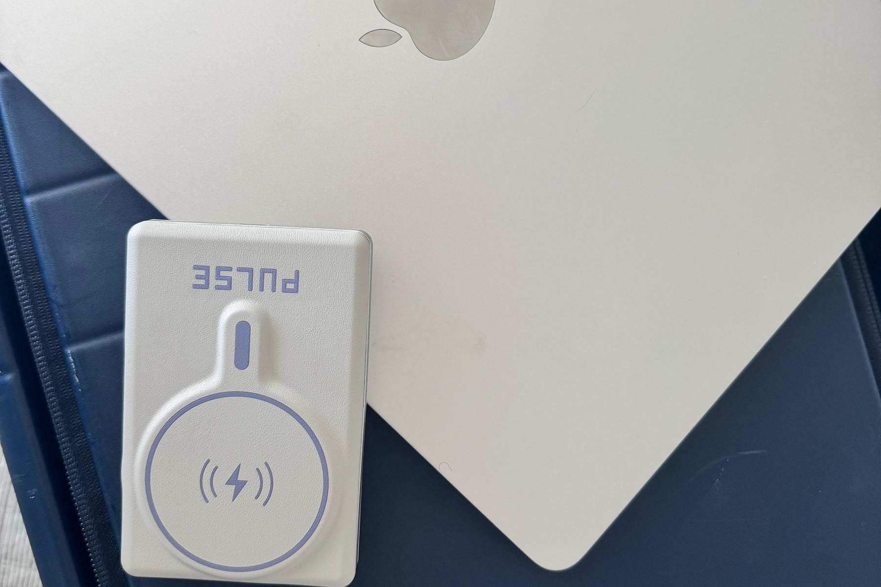 Gold MacBook and the Pulse Infinity Luxe charger resting on the Monos carry-on suitcase