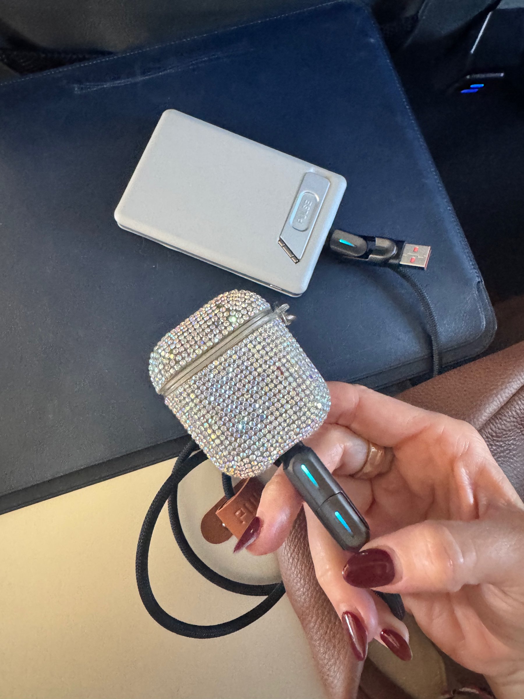 Pulse 240W charging cable and a crystal-embellished AirPods case on a plane seat tray