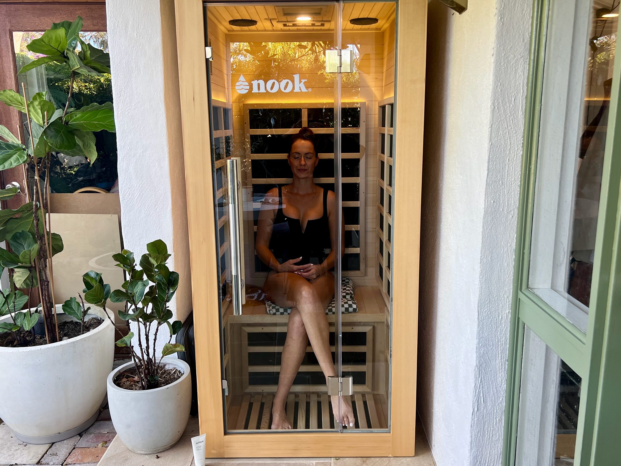 A one-person Nook Elite infrared sauna set into the nook beside a front door, with a fiddle-leaf fig on either side