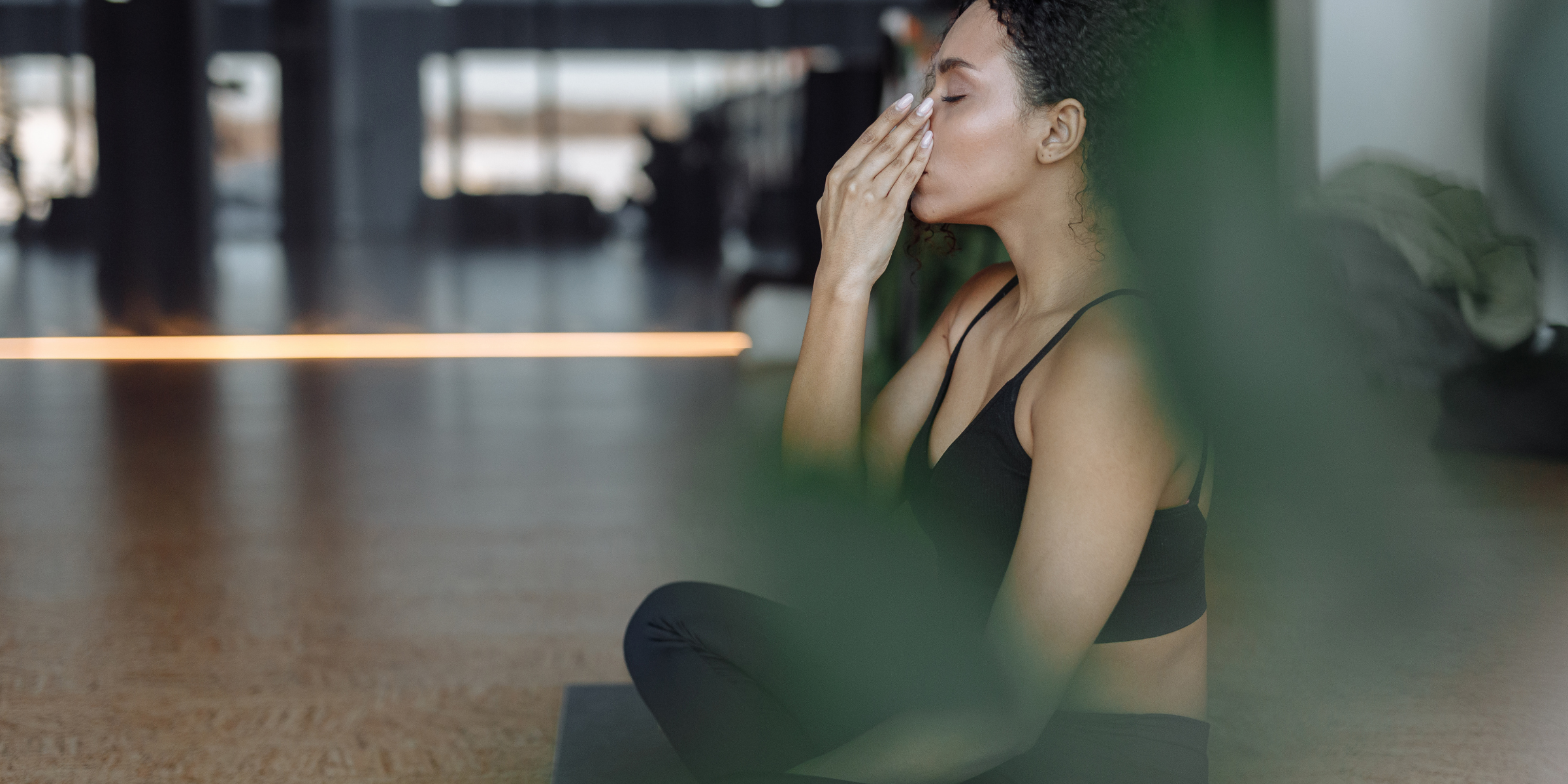 A woman practising alternate nostril breathing in a sunlit studio, eyes closed, one hand raised to her nose in a pranayama position