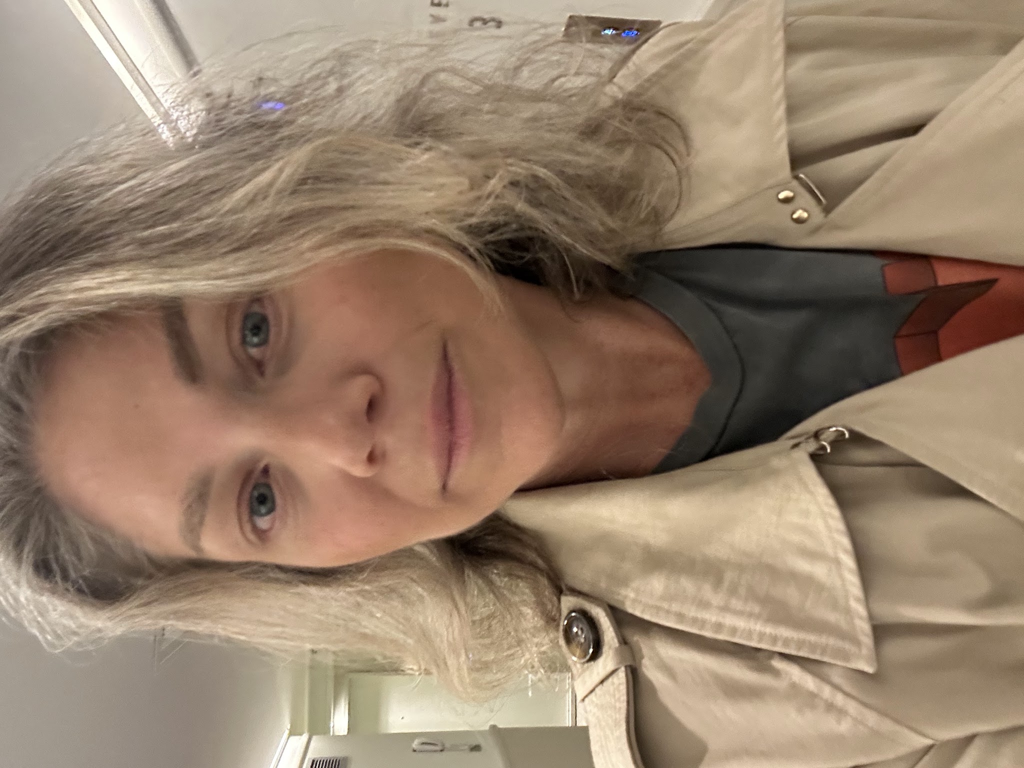 Colette in a trench coat taking a selfie, showing her hair regrowth and a quiet confidence after treatment