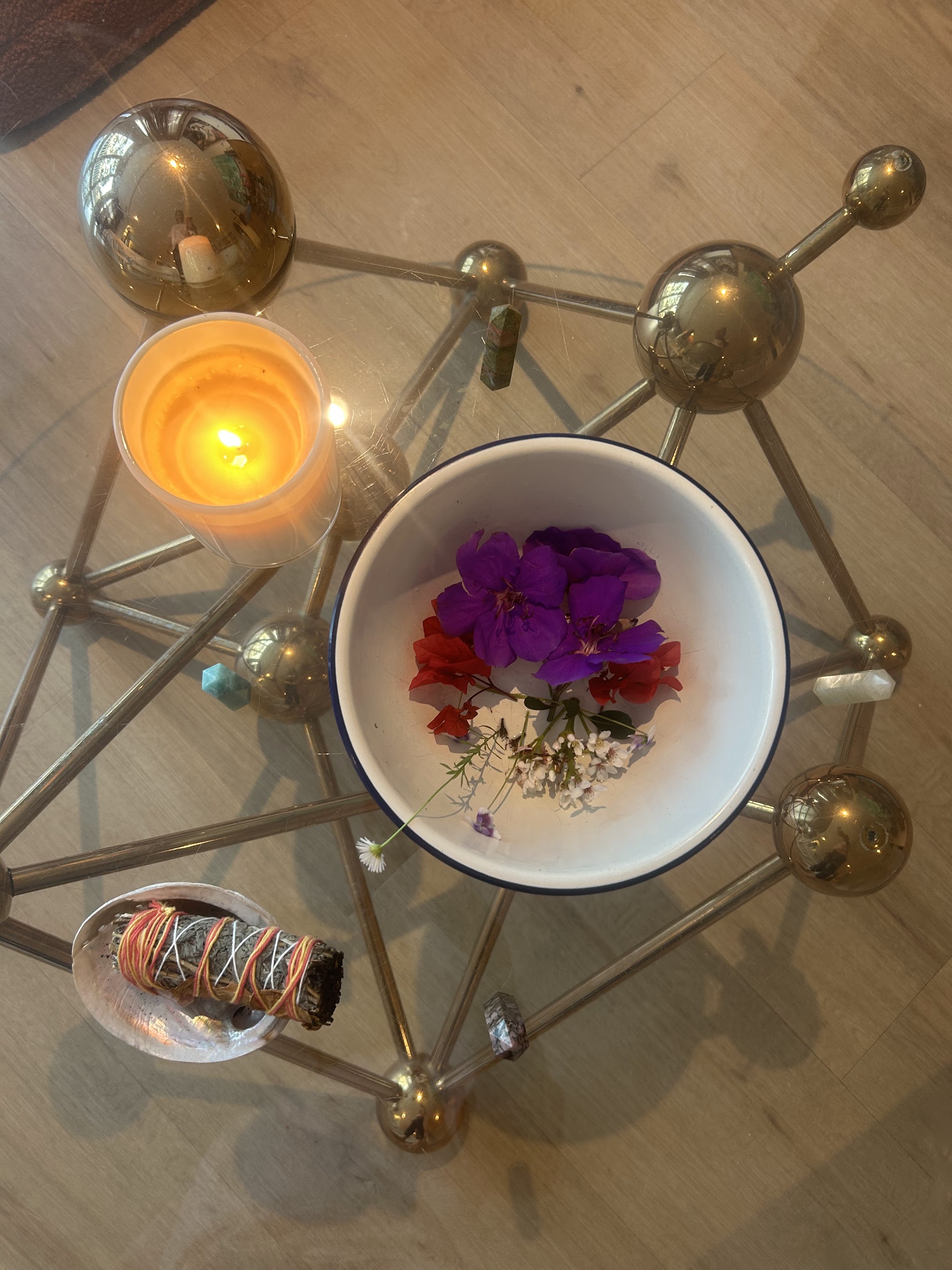 A wellness altar with a candle, fresh flowers, sage smudge stick and a golden sacred geometry structure