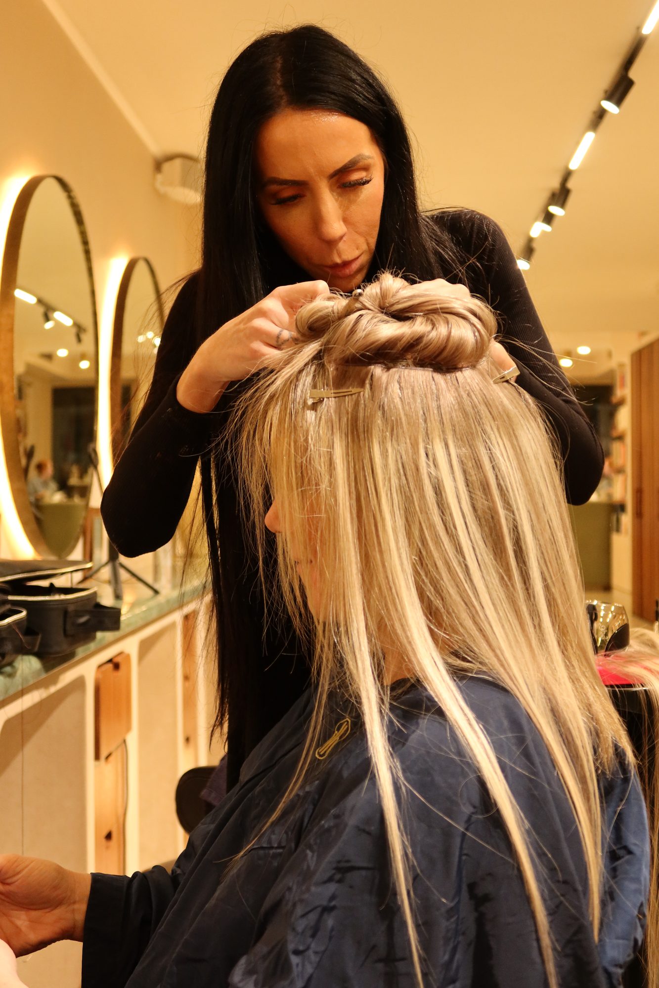 A hairdresser working extensions into Colette's blonde hair in a salon chair