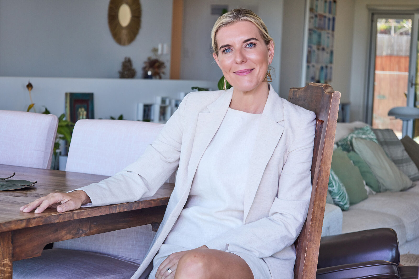 Camilla Thompson, Beauticate's Wellness Editor, seated at a timber table in a white blazer