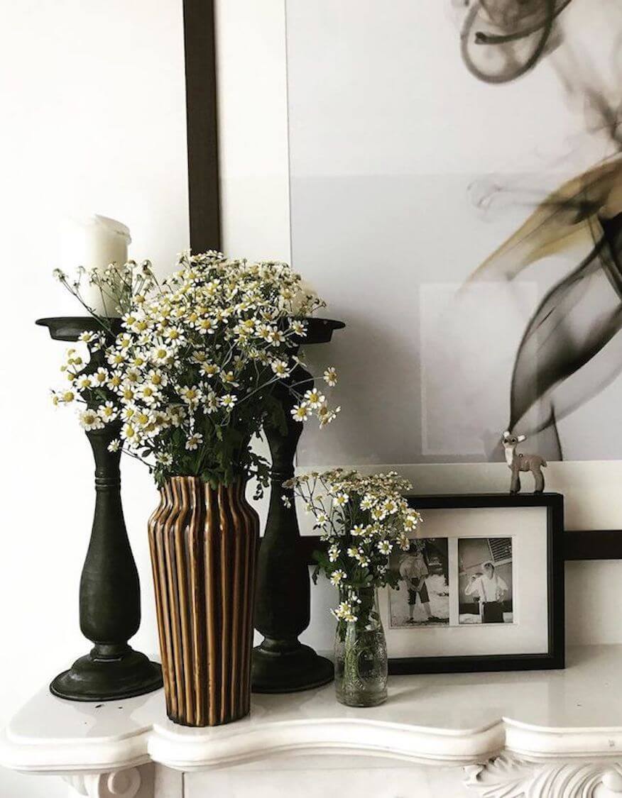 A styled vignette on Shaynna's mantelpiece with daisies in vases, candle holders and framed photographs