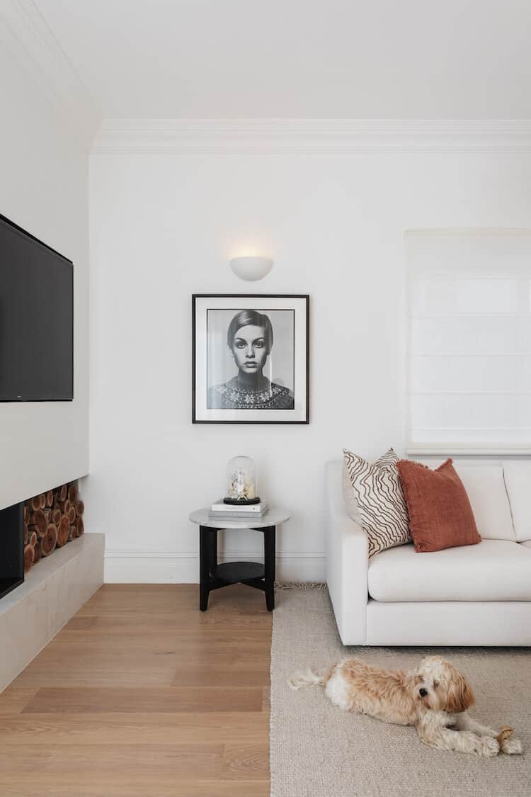 Clara's living room with framed portrait, white sofa with terracotta cushions and her cavoodle Teddy on the rug