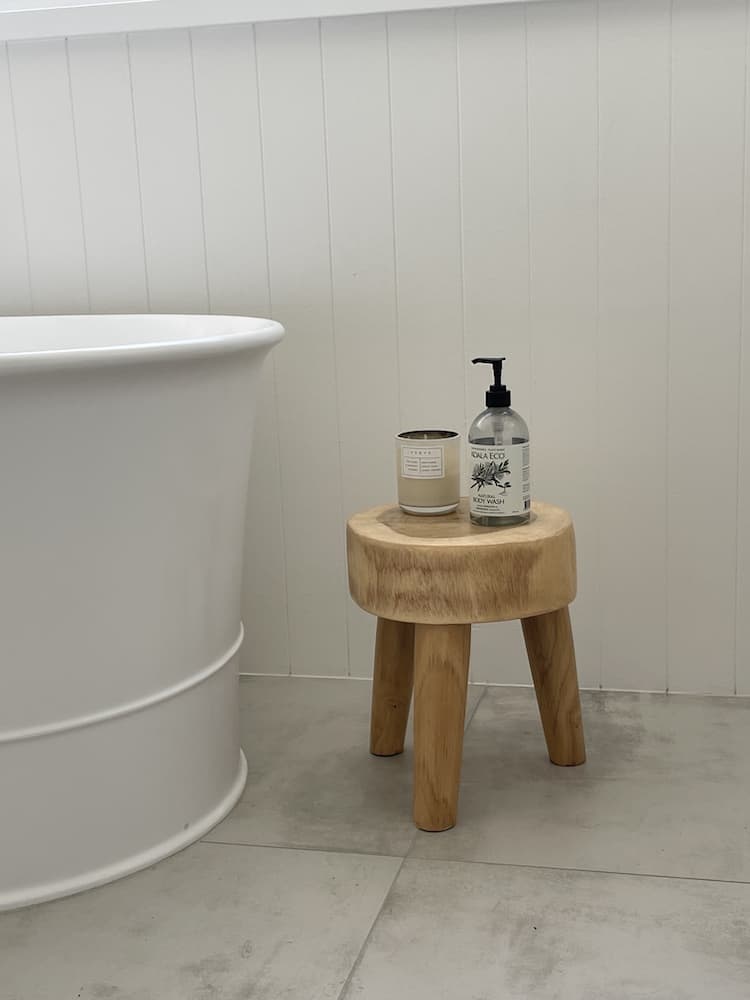 White bathroom with freestanding bath and a wooden stool holding a candle and body wash