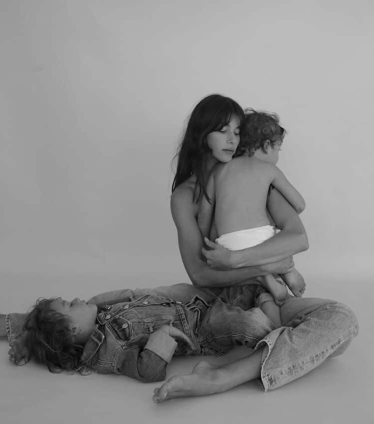 Black-and-white portrait of Helena Vestergaard in jeans holding a baby, a child lying across her lap
