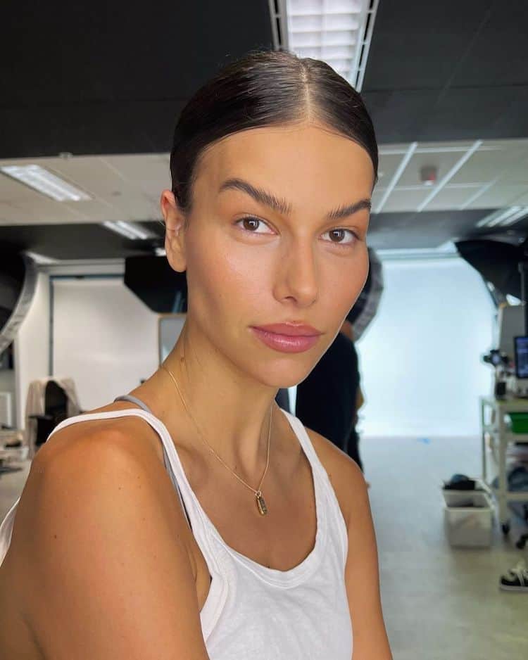 Helena Vestergaard backstage selfie in a white tank top, hair slicked back, minimal makeup, gold necklace