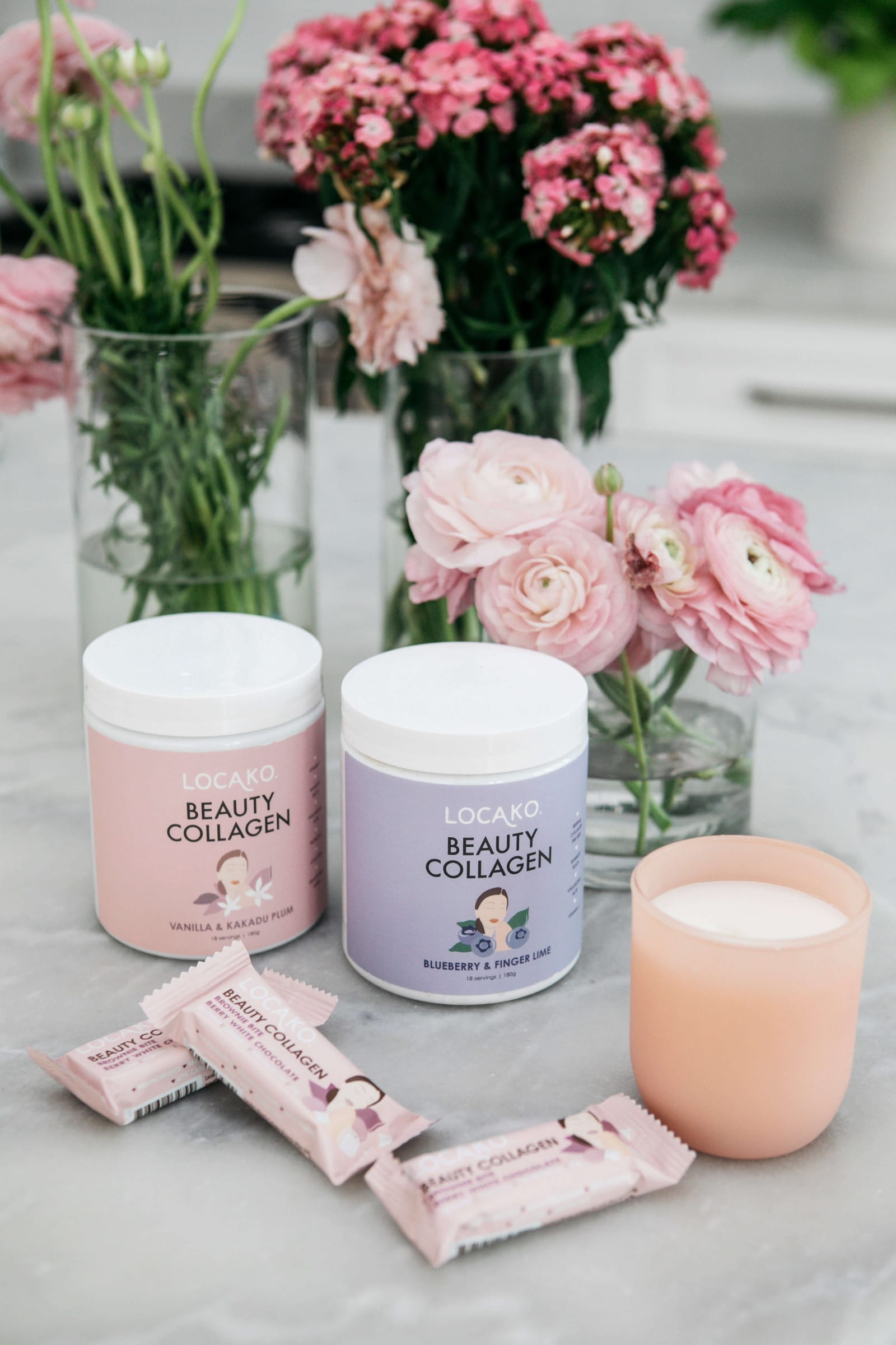 Locako Beauty Collagen tubs and bars with pink flowers and a candle on a marble benchtop