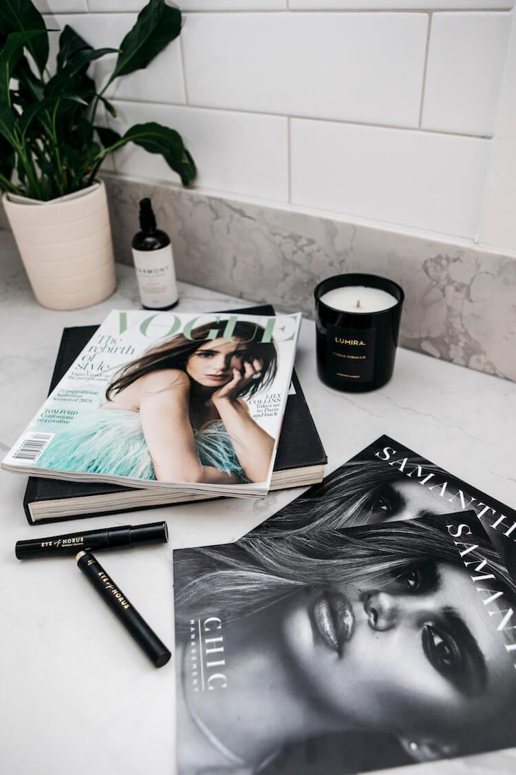 Vogue magazine, a Samantha Harris cover book, Eye of Horus mascaras and a Lumira candle on marble