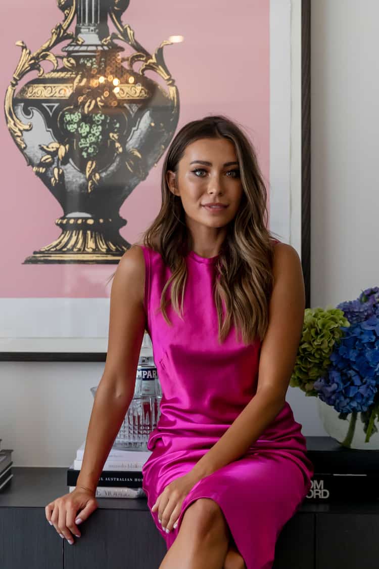 Rozalia seated on a credenza in a hot pink satin dress, Venezia vase print behind, blue and green hydrangeas