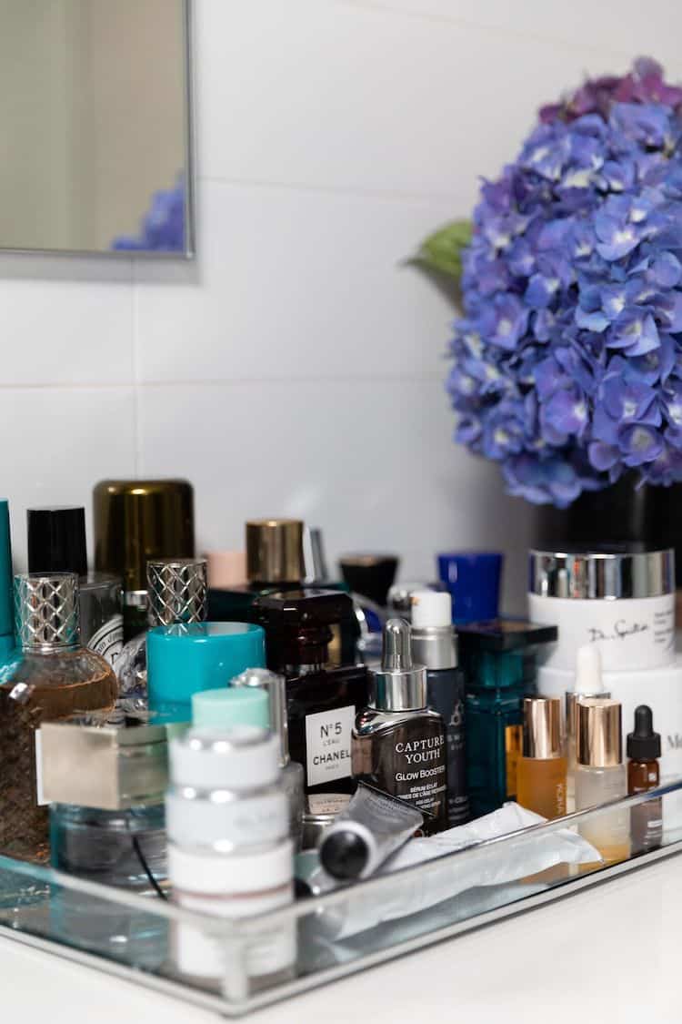 Bathroom vanity tray with skincare and fragrance including Chanel No 5, serums and purple hydrangeas