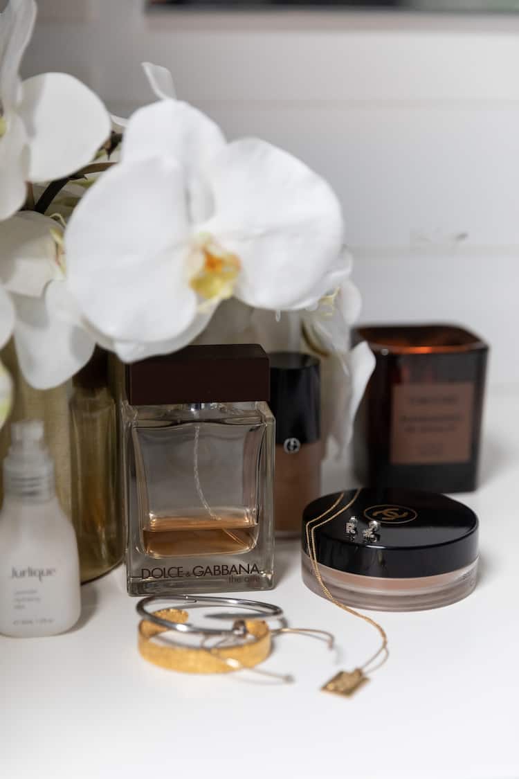 Still life with Dolce and Gabbana The One perfume, Jurlique, candle, bracelets and orchids on a white vanity