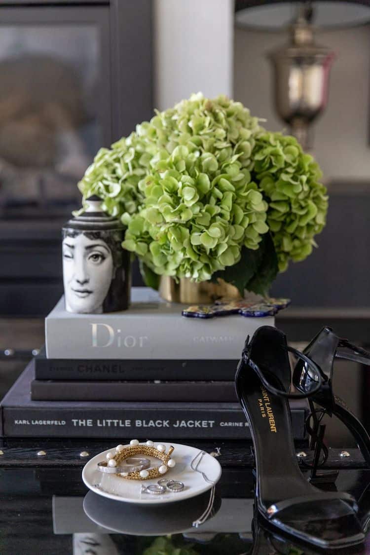 Coffee table vignette with Fornasetti candle, green hydrangeas, Dior and Chanel books, YSL heels and jewellery