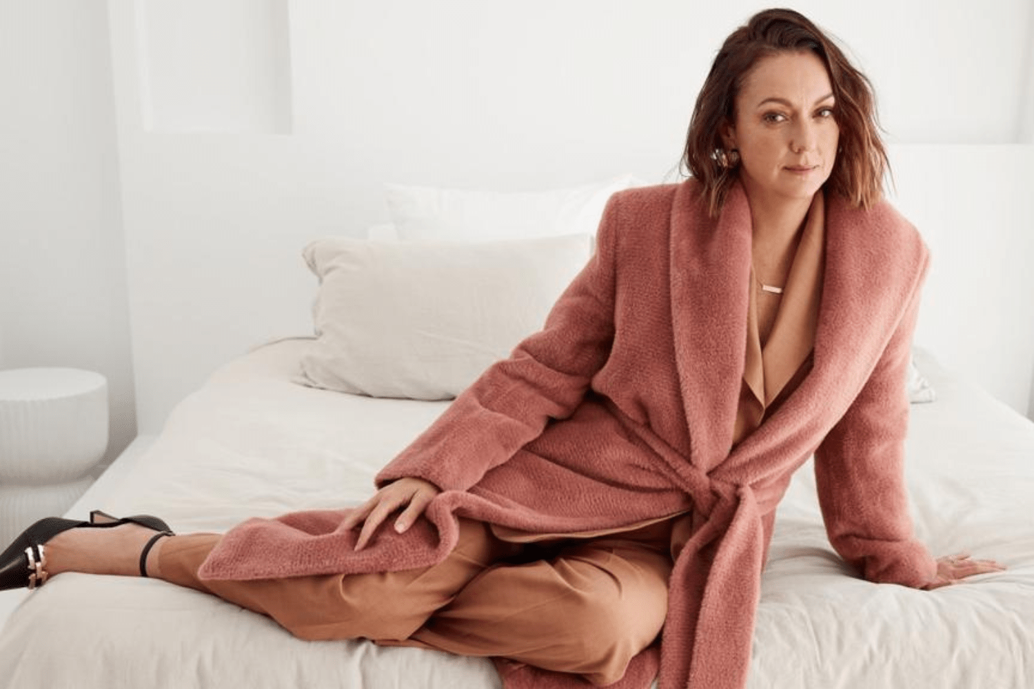 Celeste posing on bed in blush jacket