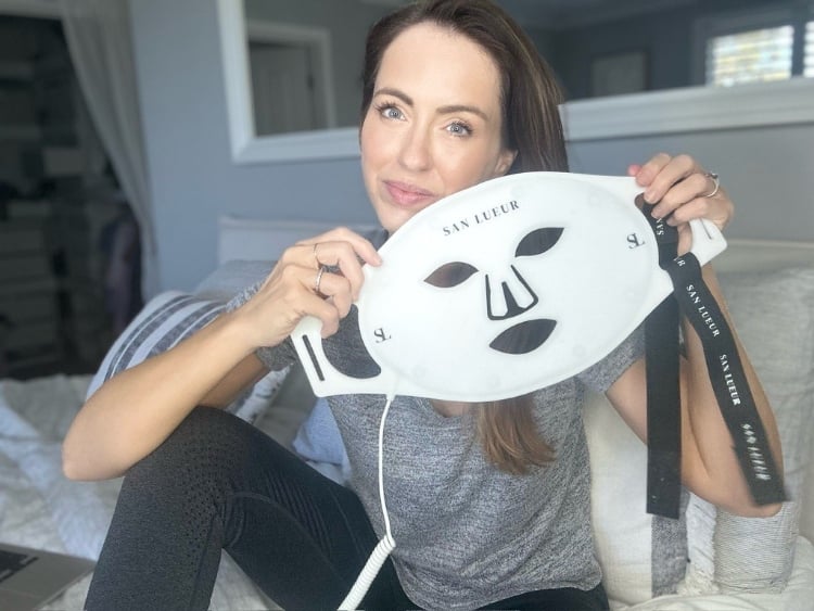 Woman wearing a red LED face mask from Sanlueur for at-home skincare and beauty treatment.