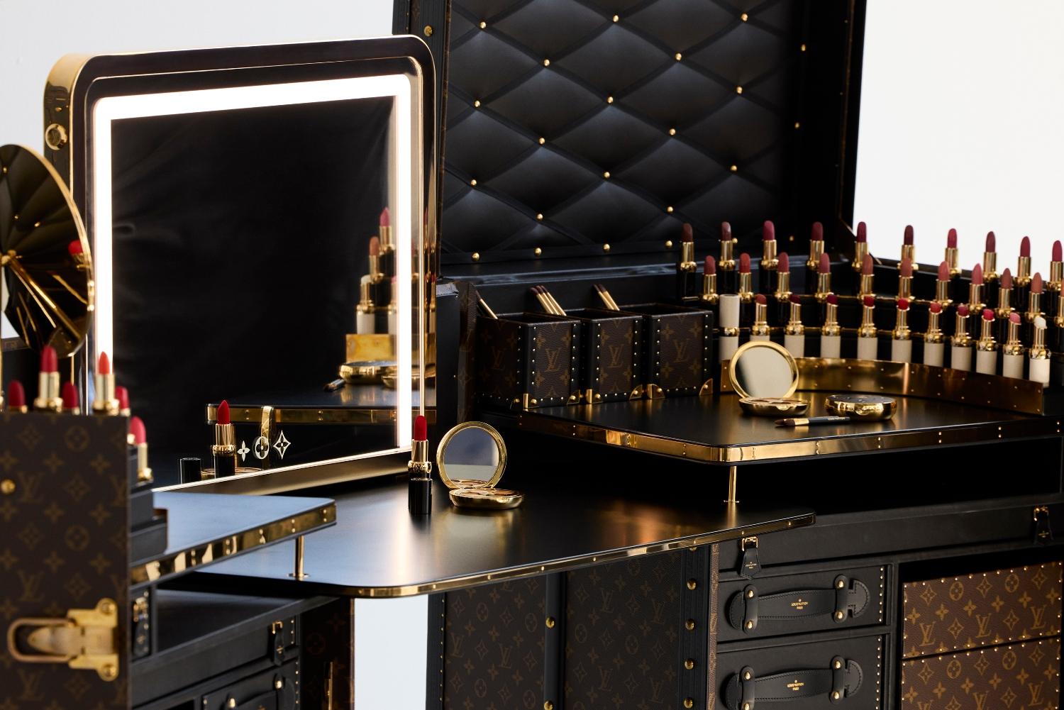 A set of Louis Vuitton cosmetics (lipstick, foundation, eyeshadow) displayed on a makeup table with Louis Vuitton monogram logo.