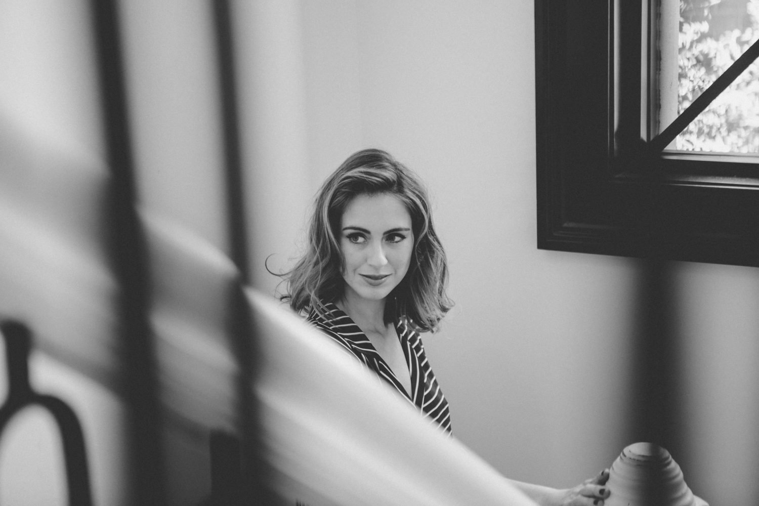 Woman with short dark hair in a black and white robe walking down wooden stairs in a softly lit, modern interior.