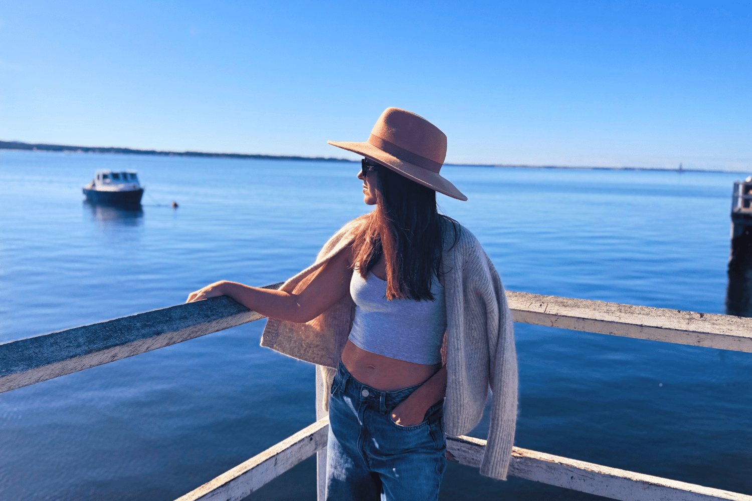 woman on pier looking at water with hat an d jacket draped on shoulder