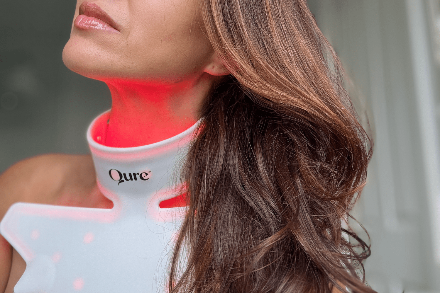 Side view of woman wearing Qure Neck & Décolletage LED Mask with red LED light illuminating the neck.